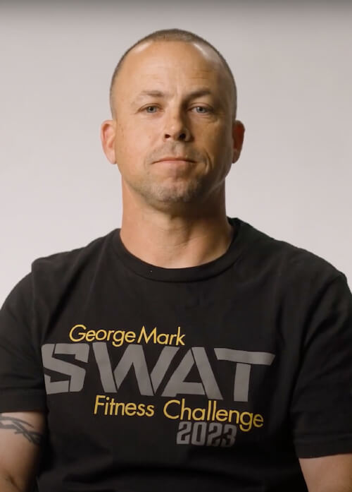 A headshot of a man in a black "SWAT" shirt