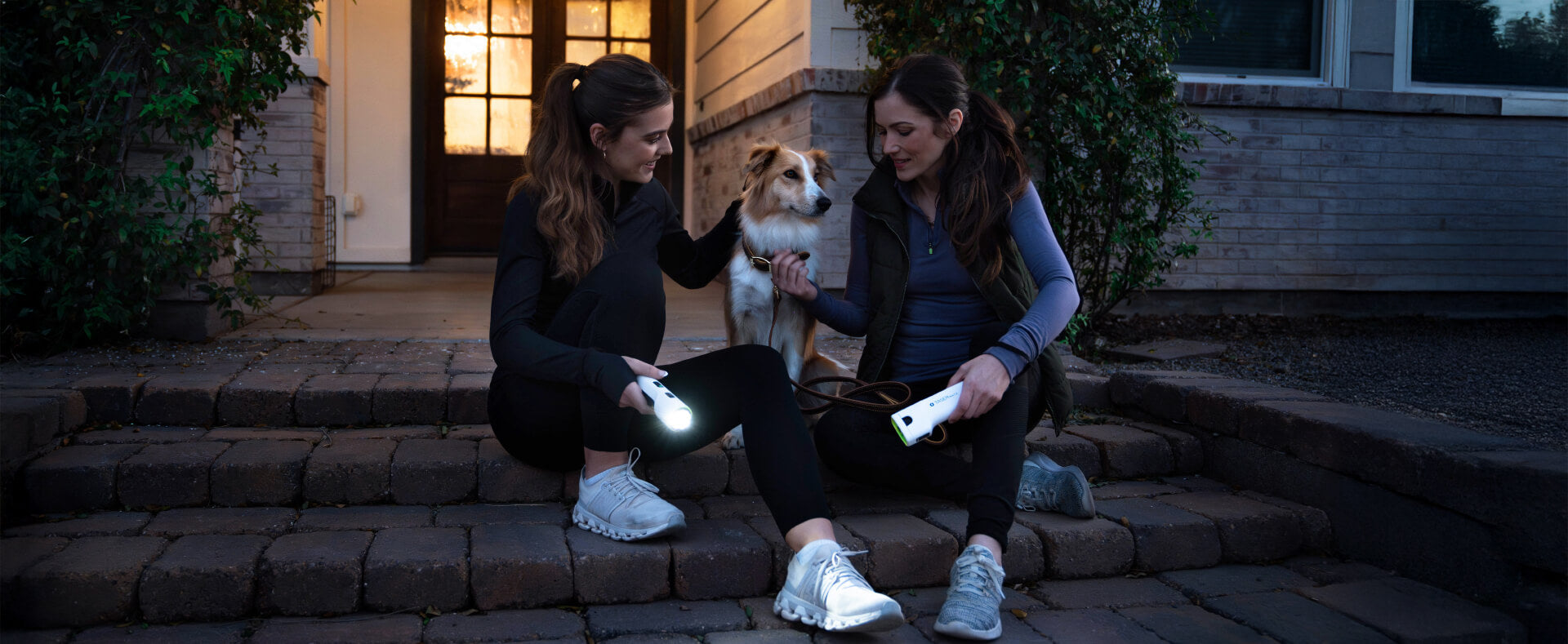 Two women on porch steps at dusk holding TASER Bolt 2 devices with a dog between them, showing everyday self-defense readiness.