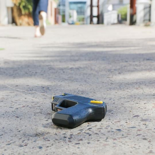TASER Pulse 2 on ground with deployed wires after use, as person runs away illustrating Safe Escape Replacement Guarantee.